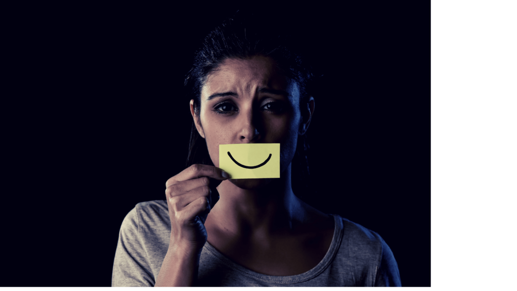 Depressed girl holding a piece of paper with a smile on it in front of her mouth 